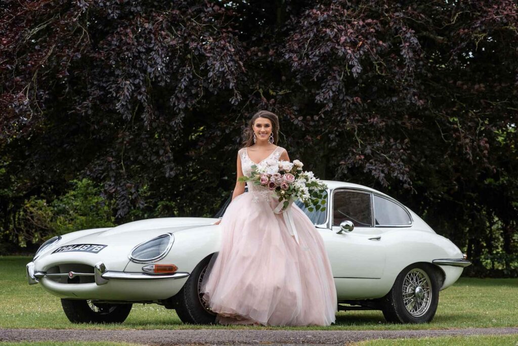 A bride in pink arriving at Bilsington Priory in an etype Jaguar