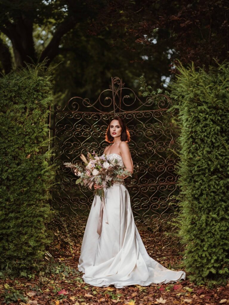 A bride stands next to a gate in the grounds of Bilsington Priory in Kent, England