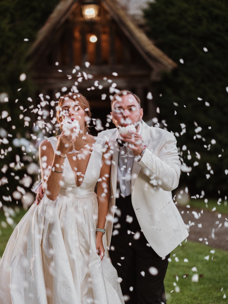 A couple blow confetti served in Champagne Flutes outside the Porch in the evening at Bilsington Priory