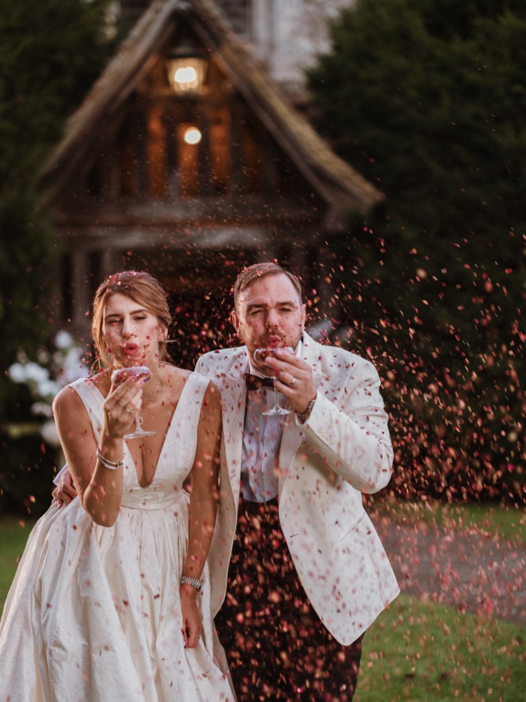 A couple blow confetti served in Champagne Flutes outside the Porch in the evening at Bilsington Priory