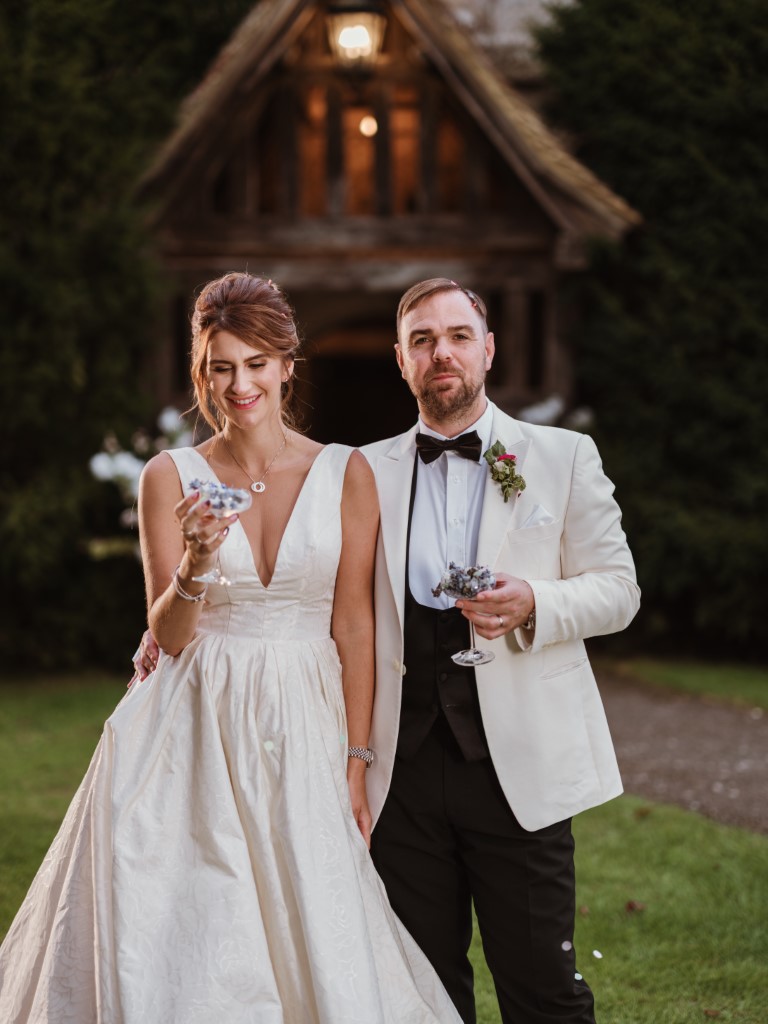 A couple get ready to blow confetti served in Champagne Flutes outside the Porch in the evening at Bilsington Priory