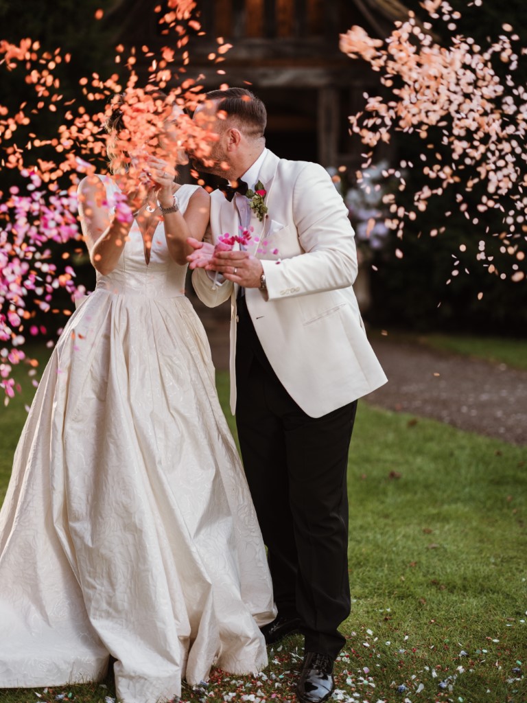 A couple pop confetti whilst kissing outside the Porch, in the evening at Bilsington Priory